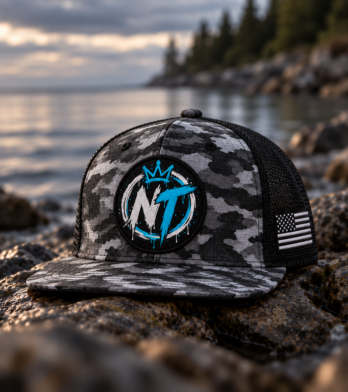 NT Camo Flatbill — camo trucker hat with NT crown patch on rocks by water